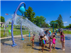 Kids gathered under tipping water bucket at splash pad