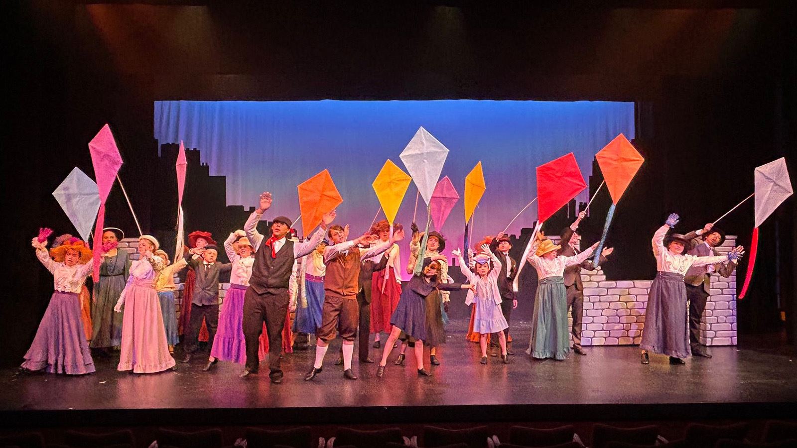 Youth performers hold kites on stage during a musical theatre production of Mary Poppins, Jr.