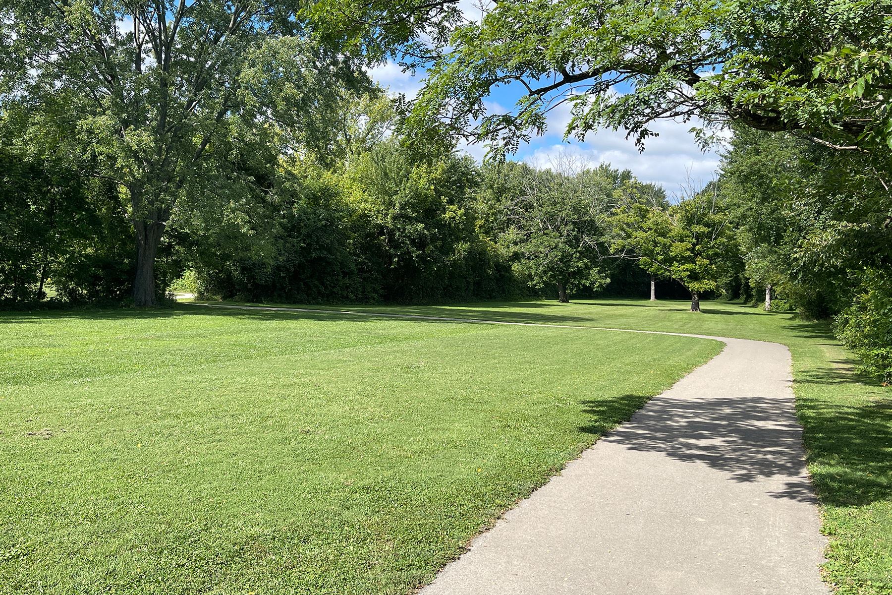 Paved walking trail winding through green lawn and wooded park area