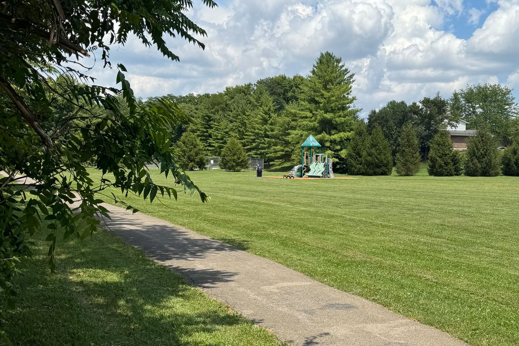 Paved walking path leading to an open field and playground.