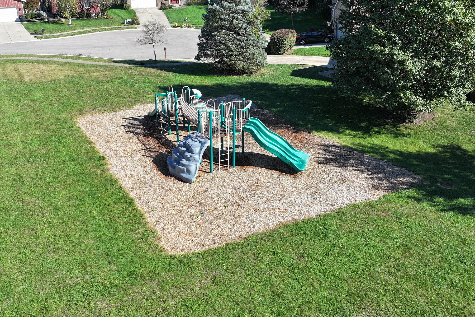 Aerial view of a playground surrounded by grass and nearby homes.